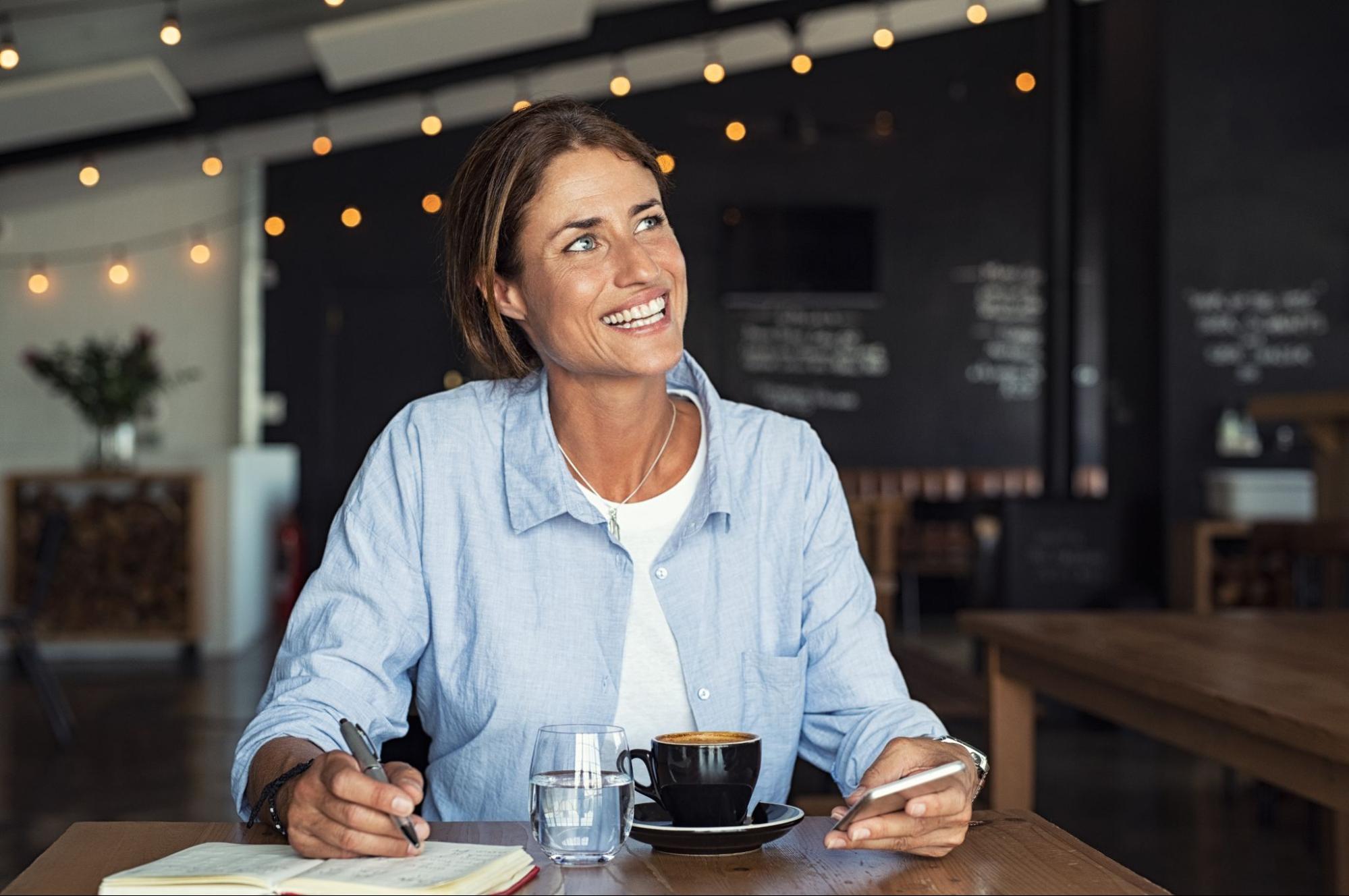 Person smiling while writing down notes inside a cafe