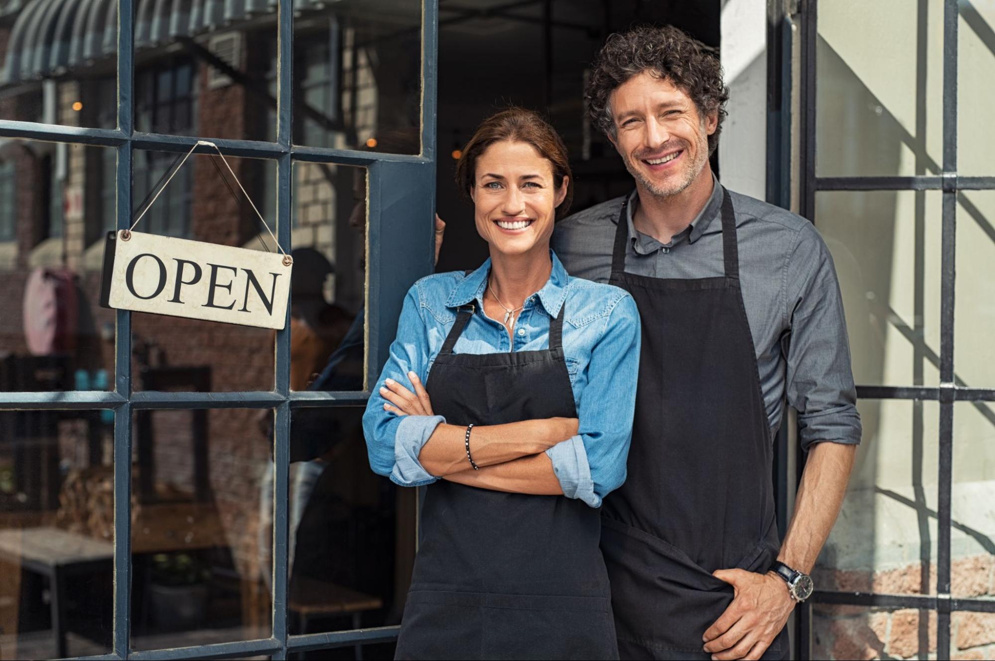 Two employees standing outside of cafe greeting customers